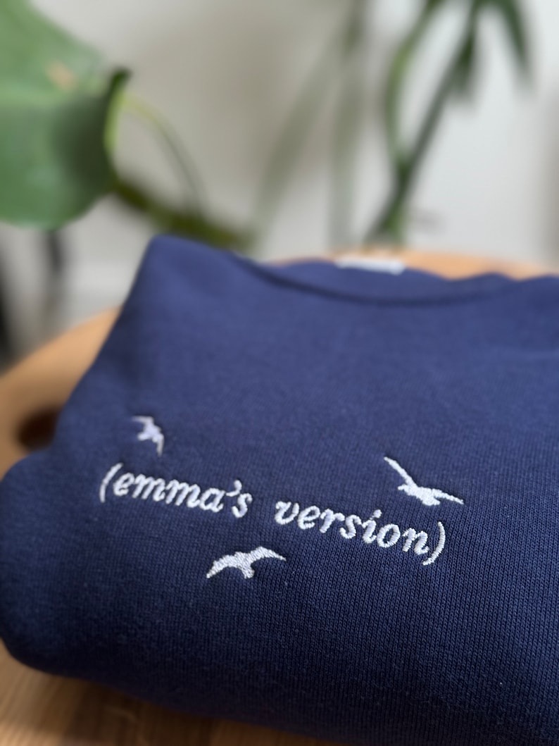 May include: A navy blue sweatshirt with white embroidered text that reads "(emma's version)" and three white embroidered birds.