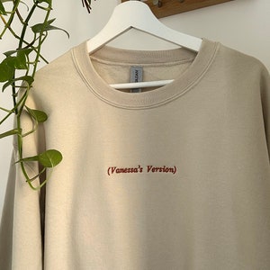 May include: A beige sweatshirt with the text "(Vanessa's Version)" embroidered in red on the front.