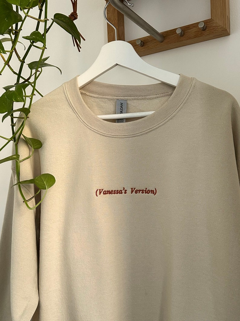 May include: A beige sweatshirt with the text "(Vanessa's Version)" embroidered in red on the front.