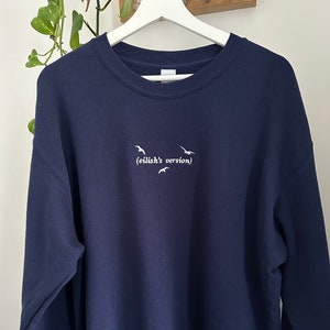 May include: A navy blue sweatshirt with white embroidered birds and the text "(eilish's version)"