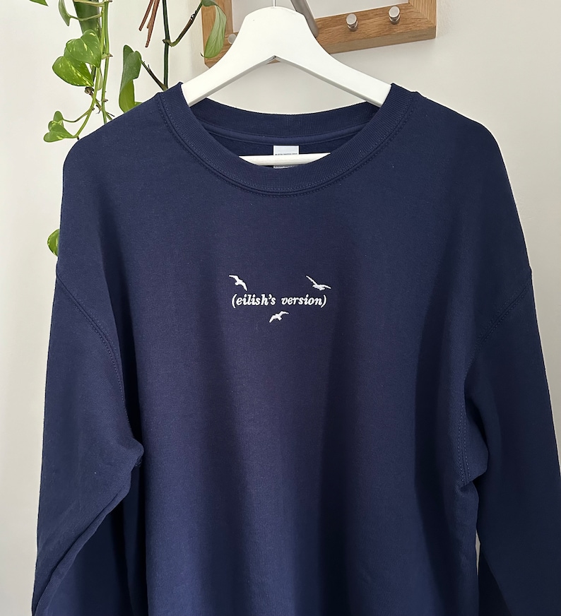 May include: A navy blue sweatshirt with white embroidered birds and the text "(eilish's version)"