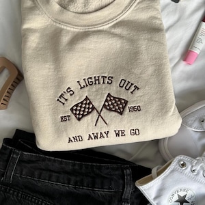 May include: Sand sweatshirt with dark brown embroidered text that reads "It's Lights Out Est. 1950 And Away We Go" with a chequered flag graphic.
