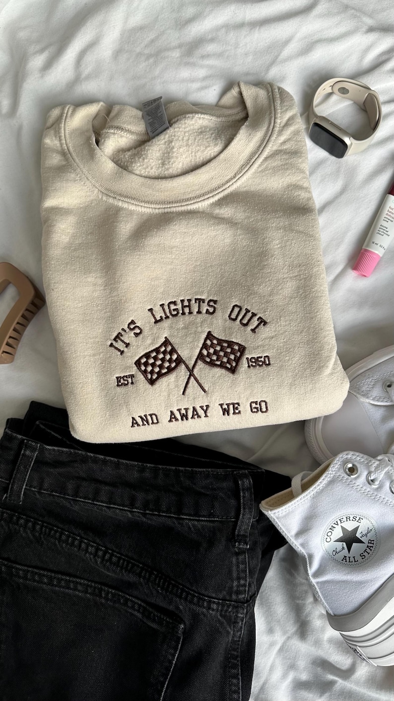 May include: Sand sweatshirt with dark brown embroidered text that reads "It's Lights Out Est. 1950 And Away We Go" with a chequered flag graphic.