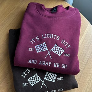 May include: Brugundy and black sweatshirt with white embroidered text that reads "It's Lights Out Est. 1950 And Away We Go" with a chequered flag graphic.