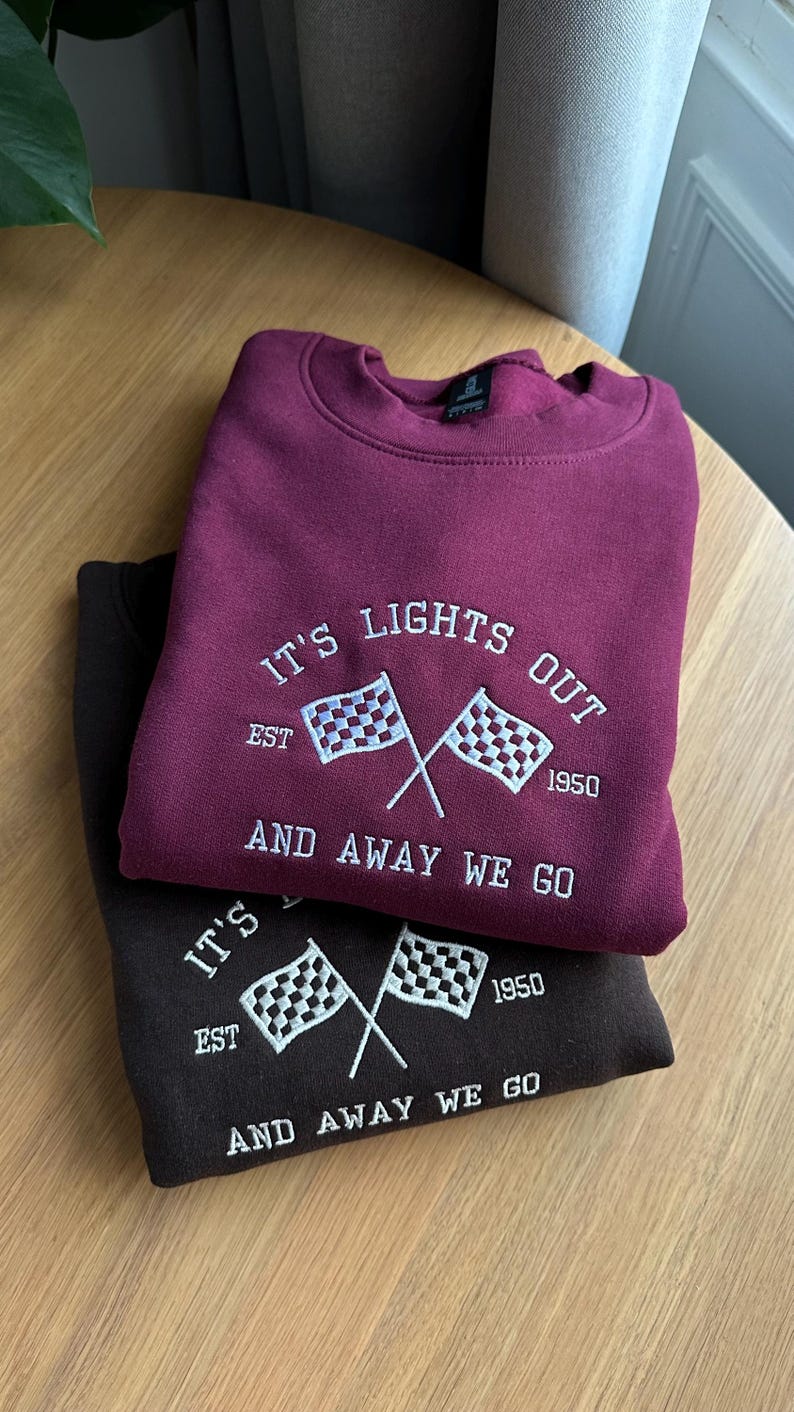 May include: Brugundy and black sweatshirt with white embroidered text that reads "It's Lights Out Est. 1950 And Away We Go" with a chequered flag graphic.