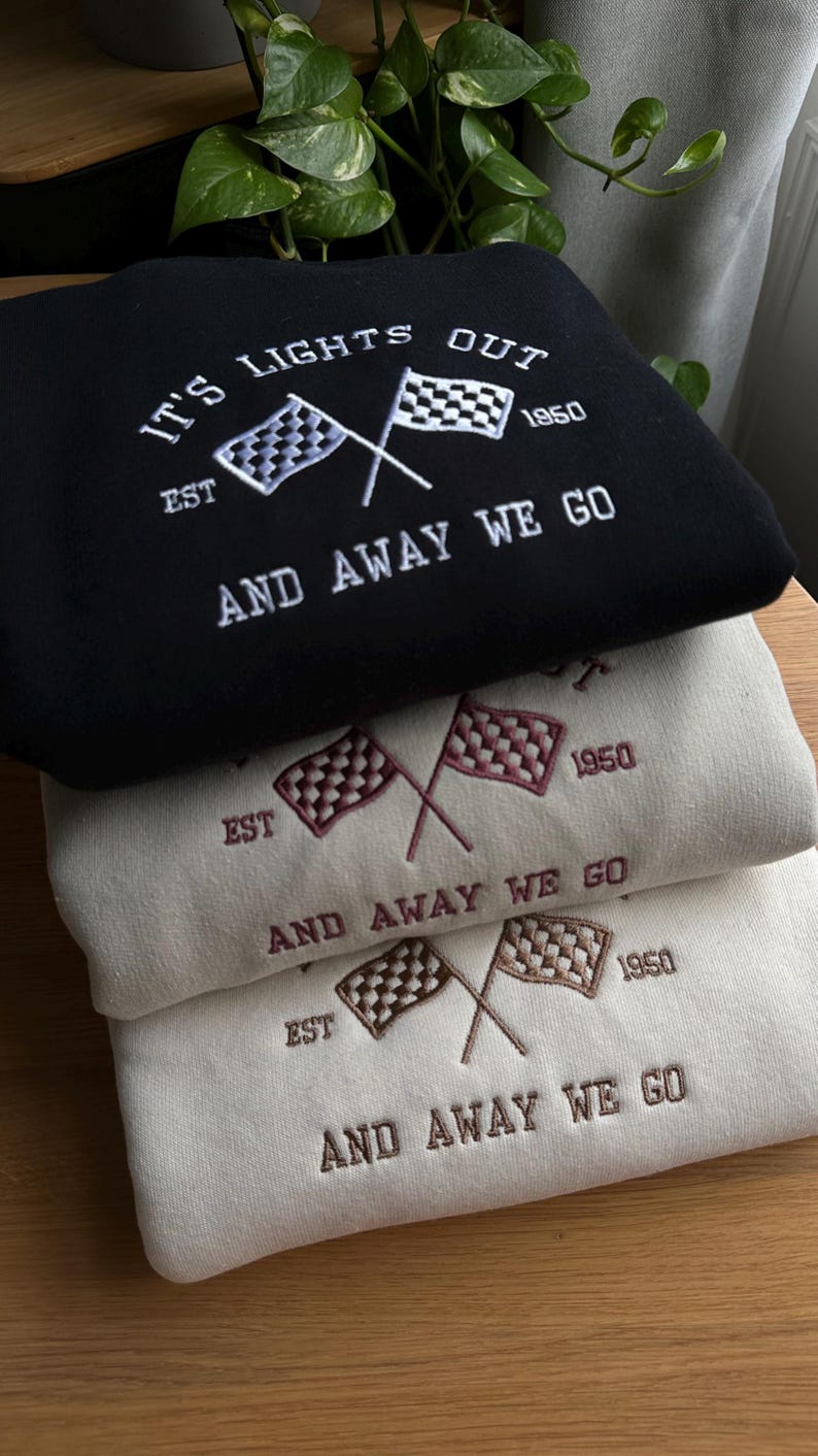 K&ouml;nnte beinhalten: Drei Sweatshirts &uuml;bereinander gestapelt. Das oberste Sweatshirt ist schwarz mit wei&szlig;er Stickerei, die "IT'S LIGHTS OUT EST 1950 AND AWAY WE GO" lautet. Das mittlere Sweatshirt ist beige mit burgunderfarbener Stickerei, die "EST 1950 AND AWAY WE GO" lautet. Das unterste Sweatshirt ist beige mit brauner Stickerei, die "EST 1950 AND AWAY WE GO" lautet.
