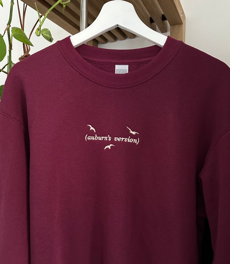 May include: Burgundy sweatshirt with a white embroidered design of birds flying and the text "(auburn's version)"