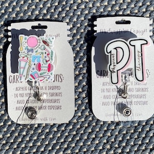 Puede incluir: Dos etiquetas rectangulares de cartulina blanca con esquinas redondeadas. Cada etiqueta tiene un fondo blanco con texto negro y un gráfico colorido. La etiqueta de la izquierda tiene un gráfico de una mancuerna rosa, una esterilla de yoga azul, una pelota de ejercicio verde y amarilla, un bastón rosa y blanco y otros artículos relacionados con el fitness. La etiqueta de la derecha tiene un gráfico de las letras "PT" en rosa y blanco con las palabras "Fisioterapia" escritas en negro. Ambas etiquetas tienen un carrete de insignia retráctil plateado unido a ellas.