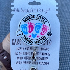 Könnte beinhalten: Ein runder Ausweishalter mit weißem Hintergrund, blauen und rosa Babyfußabdrücken und dem Text "WHERE LITTLE NICU THINGS MATTER". Der Ausweishalter ist auf einer weißen Karte mit dem Text "Midwestern Design" und Pflegehinweisen befestigt.