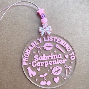 May include: Pink acrylic keychain with the text "Probably Listening to Sabrina Carpenter" and pink hearts, cherries, lips, stars, bows, and a shoe.