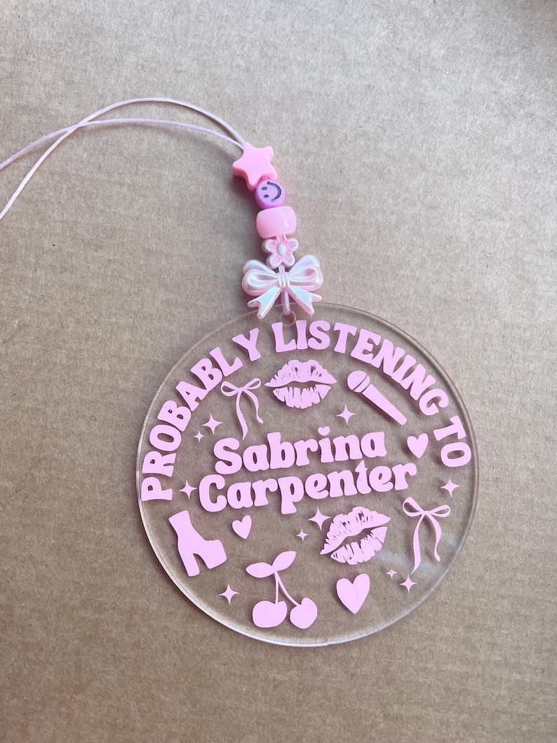May include: Pink acrylic keychain with the text "Probably Listening to Sabrina Carpenter" and pink hearts, cherries, lips, stars, bows, and a shoe.