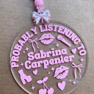 May include: Pink acrylic keychain with the text "Probably Listening to Sabrina Carpenter" and pink hearts, lips, cherries, a shoe, and a microphone.