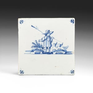 May include: Square white ceramic tile with a blue and white illustration of a person in a hat holding a long pole. The person is standing in front of a bush. Floral designs are in each corner.