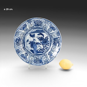 Puede incluir: Un plato de cerámica azul y blanco con un diseño floral y de mariposas. El plato tiene aproximadamente 29 cm de diámetro. Un limón amarillo está a la derecha del plato.