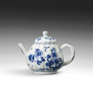 May include: A white porcelain teapot with a blue floral design. The teapot has a rounded body, a curved spout, and a loop handle. The lid is topped with a small knob. The blue floral pattern decorates the body and lid.