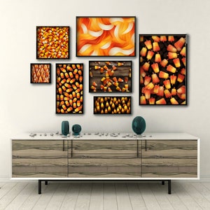 May include: A set of seven framed prints featuring various patterns of candy corn. The prints are arranged in a grid on a white wall above a wooden cabinet.