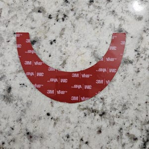May include: A red adhesive tape strip with the text "3M VHB" repeated multiple times. The tape is curved in a U-shape.