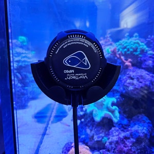 May include: Black VorTech MP60 propeller pump for aquariums. The pump has a circular design with a fish graphic and the text "VorTech" and "MP60". The pump is mounted inside a glass aquarium with colorful coral and plants.