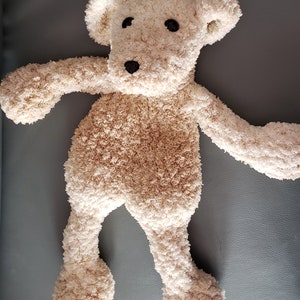 May include: A beige plush teddy bear with black eyes and a black nose. The bear is lying on its back with its arms and legs outstretched.