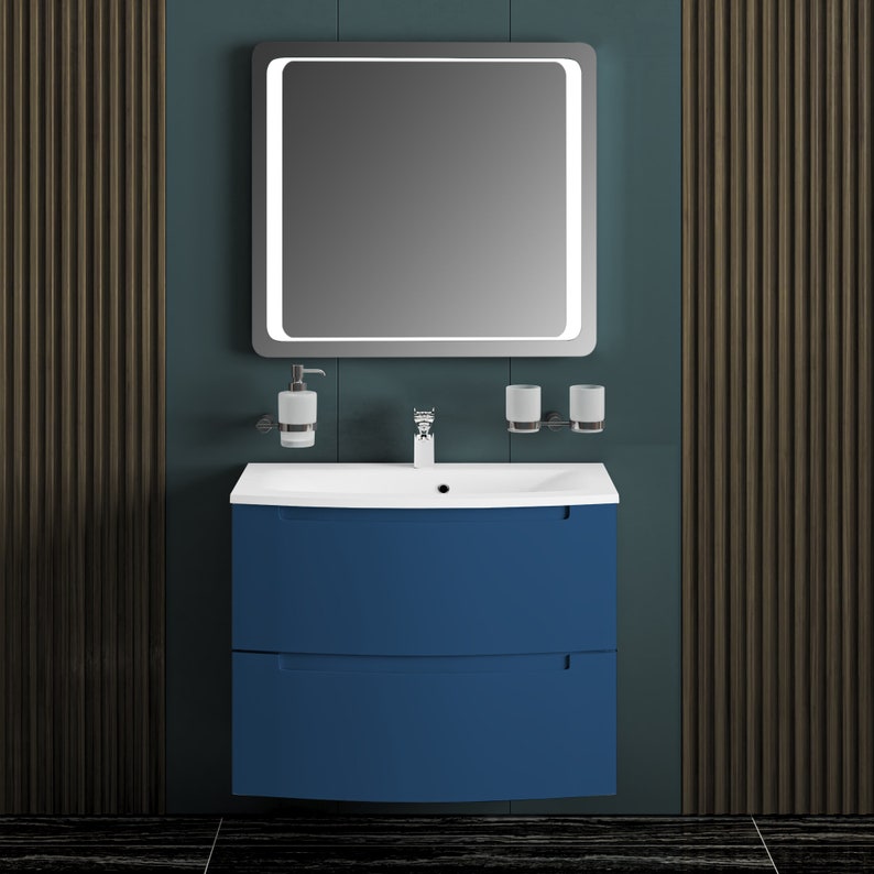 Puede incluir: Un tocador de ba&ntilde;o azul con dos cajones y un lavabo de porcelana blanca. El tocador tiene un frente curvo y est&aacute; montado en la pared. Un espejo con una luz alrededor del per&iacute;metro est&aacute; montado sobre el tocador.