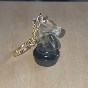 May include: A clear glass chess knight keyring with a black base and a gold chain.