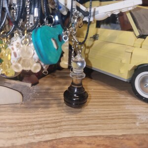 May include: A black and clear glass chess piece pendant hanging from a silver chain. The pendant is shaped like a chess pawn and has a clear glass top. The pendant is hanging from a silver chain and is surrounded by other jewellery.