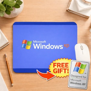 May include: A blue mousepad featuring the Microsoft Windows XP logo, with a white mouse to the right. A "FREE GIFT!" sticker and a "Designed for Microsoft Windows XP" sticker are also present.