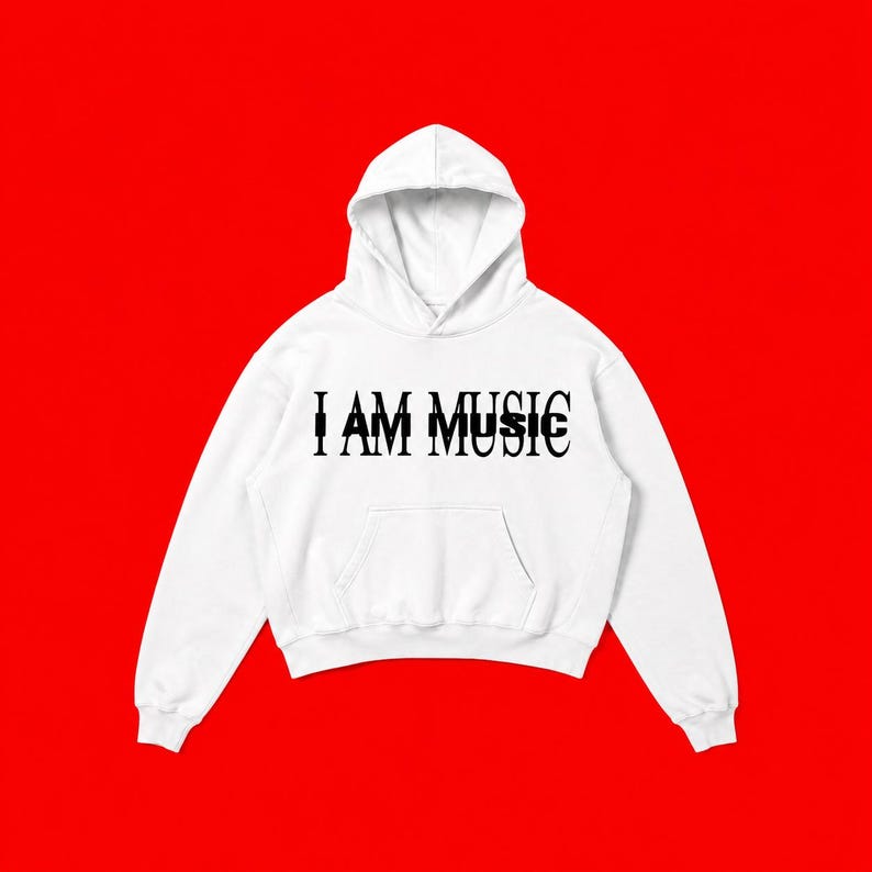 May include: A white hooded sweatshirt featuring a front kangaroo pocket and long sleeves. The chest displays the text I AM MUSIC printed in a bold black serif font, with a secondary overlapping black text effect creating a layered visual.
