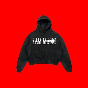 May include: A black hooded sweatshirt featuring a front kangaroo pocket and the white text I AM MUSIC printed across the chest. The garment has long sleeves with ribbed cuffs and a matching ribbed hem, constructed from a solid black fabric.