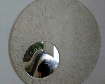 Peut inclure: Un miroir rond de couleur argentée avec une surface texturée. Le miroir a un miroir rond plus petit au centre, reflétant une personne et une pièce.