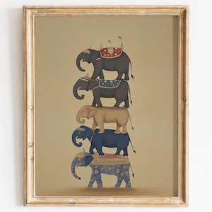 May include: A framed print depicting a tower of five elephants, each with ornate saddle blankets. The elephants are in shades of grey, tan, and blue, set against a neutral backdrop. The frame is a light gold colour.