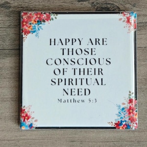 May include: Square white plaque with the text "HAPPY ARE THOSE CONSCIOUS OF THEIR SPIRITUAL NEED Matthew 5:3". The corners are decorated with floral arrangements in red, blue, and yellow.
