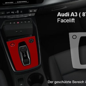 Può includere: Vista interna di un'Audi A3 (8Y) Facelift. La console centrale presenta un pannello rosso che evidenzia il cambio e i comandi. L'immagine mostra anche una sovrapposizione grigia e il logo SEcoverline.