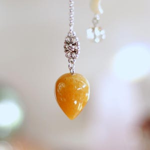 Könnte beinhalten: Silberne Kettenohrringe mit einem tropfenförmigen, orange-gelben Edelsteinanhänger. Der Ohrring hat auch einen kleinen floralen Akzent und eine zweite Kette mit einem Mond- und Stern-Charm. Der Hintergrund ist verschwommen.