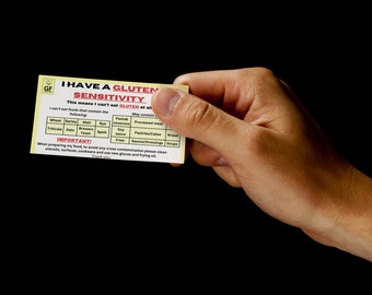 May include: A yellow and white card with the text "I have a gluten sensitivity" and a table listing foods that contain gluten. The card is being held by a hand.