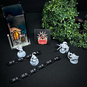May include: A top-down view shows miniature figurines, distance markers, and a decorative building. The figurines are grey, and the black distance markers have white text indicating distances in feet. A square card with "ZIKGEEK GUILD" is also present.