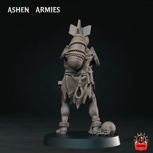 May include: A gray miniature figurine of a humanoid character standing on a circular base. The figure wears tattered clothing, carries a large bomb strapped to its back with rope, and has a ball and chain attached to one ankle. Text reads ASHEN ARMIES.