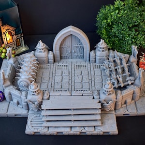 Może przedstawiać: Szara miniaturowa brama do lochu z drewnianymi drzwiami, kamiennymi schodami i drabiną. Scena zawiera elementy dekoracyjne, takie jak kolczaste bariery i konstrukcje przypominające pochodnie, idealne do gier stołowych. Widoczna jest fioletowa kostka do gry.