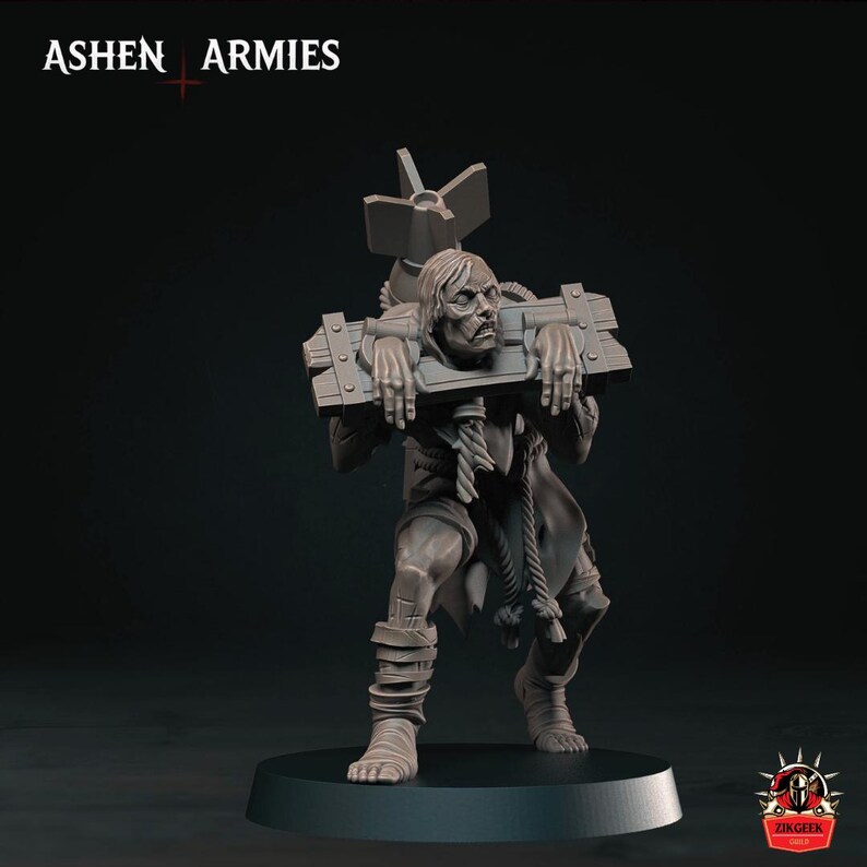 May include: A gray miniature figure of a person locked in wooden stocks, carrying a large bomb on their back. The figure has ropes tied around their neck and waist, with text reading ASHEN ARMIES at the top and ZIKGEEK at the bottom right.