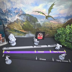 May include: Three distance measuring tools for tabletop gaming. The tools are gray, purple, and black, each with white text indicating distance. Miniature figurines and a dragon backdrop are also visible.