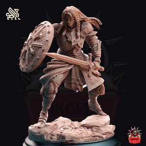 Może przedstawiać: Szczegółowa miniatura przedstawiająca wojowniczkę w pozycji obronnej, trzymającą miecz i tarczę. Figurka wykonana jest z jasnobrązowego materiału i pomalowana w realistycznym stylu.