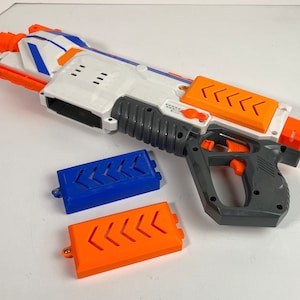 May include: A white, blue, and orange toy gun with a gray handle and two orange and blue clips. The gun has a textured surface and a trigger.