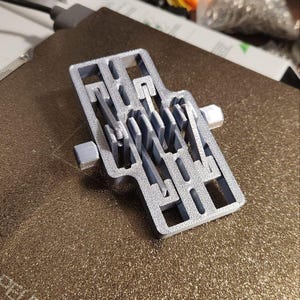 May include: A silver-colored 3D printed object with a complex, interlocking design. The object has a textured surface and appears to be made of plastic.