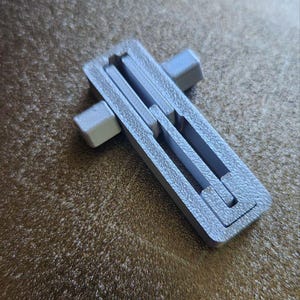 May include: A silver metal cross-shaped object with a textured surface. The object is made of multiple pieces that fit together.