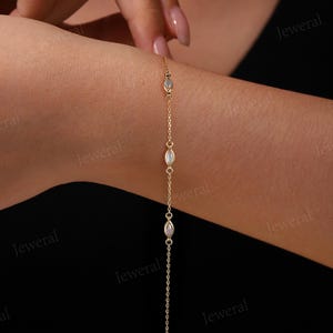 May include: A delicate gold bracelet featuring a chain design with three oval-shaped, iridescent gemstones. The bracelet is shown on a wrist, with the gemstones spaced along the chain. The bracelet is a piece of jewelry.