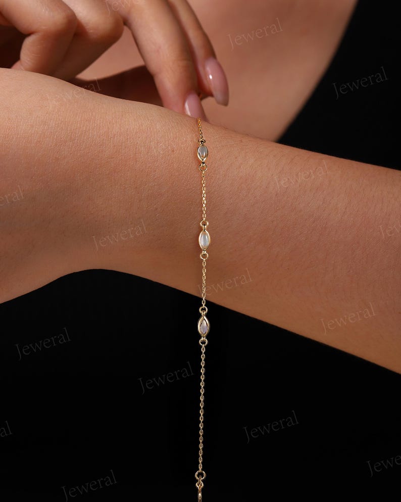 May include: A delicate gold bracelet featuring a chain design with three oval-shaped, iridescent gemstones. The bracelet is shown on a wrist, with the gemstones spaced along the chain. The bracelet is a piece of jewelry.