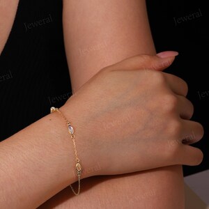 May include: A delicate gold bracelet featuring oval-shaped gemstones and small round accents. The bracelet is worn on a wrist, showcasing its fine chain and the subtle sparkle of the stones. The design is simple yet elegant, suitable for everyday wear or special occasions.