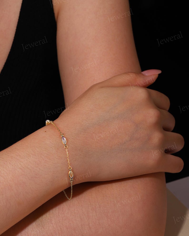 May include: A delicate gold bracelet featuring oval-shaped gemstones and small round accents. The bracelet is worn on a wrist, showcasing its fine chain and the subtle sparkle of the stones. The design is simple yet elegant, suitable for everyday wear or special occasions.