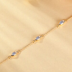 May include: A delicate gold-colored chain bracelet featuring four oval-shaped, iridescent gemstones. The bracelet is set against a soft, neutral background, highlighting the jewelry's subtle elegance. This piece is suitable for everyday wear or special occasions.
