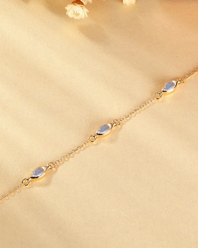 May include: A delicate gold-colored chain bracelet featuring four oval-shaped, iridescent gemstones. The bracelet is set against a soft, neutral background, highlighting the jewelry's subtle elegance. This piece is suitable for everyday wear or special occasions.
